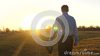Un homme d'affaires avec une mallette se rend au beau coucher du soleil après la journée de travail agronome traverse le champ de banque de vidéos Un homme d'affaires avec une mallette se rend au beau coucher du soleil après la journée de travail agronome traverse le champ de banque de vidéos