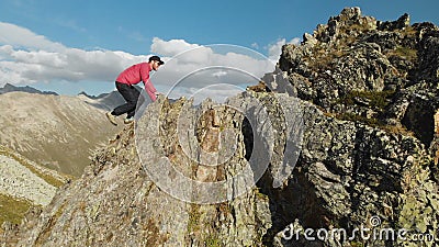 Un jeune type avec une barbe, un alpiniste dans un chapeau et les lunettes de soleil, monte une haute rocheuse d'arête dans les m banque de vidéos Un jeune type avec une barbe, un alpiniste dans un chapeau et les lunettes de soleil, monte une haute rocheuse d'arête dans les m banque de vidéos