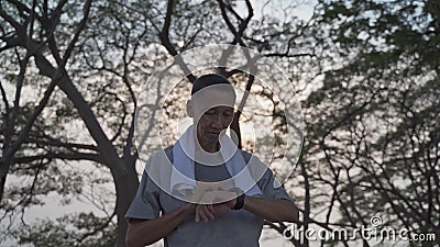 Un vieil homme asiatique touche un moniteur d'activité smart watch au parc sous un arbre. finger tapping sport montre pour les cal banque de vidéos Un vieil homme asiatique touche un moniteur d'activité smart watch au parc sous un arbre. finger tapping sport montre pour les cal banque de vidéos
