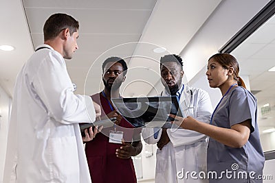 Unaltered portrait of four serious diverse doctors with table, x ray talking in hospital corridor Stock Photo
