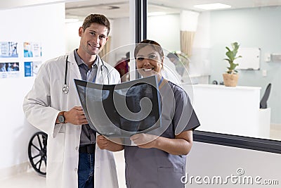 Unaltered portrait of happy diverse male and female doctor looking at x ray in hospital corridor Stock Photo