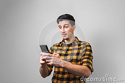 Unbelievable happy news. surprised man in yellow shirt holding a phone on grey background Stock Photo