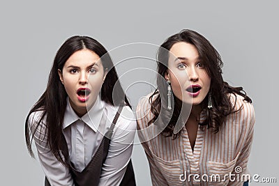 Unbelievable news. Closeup portrait of shocked beautiful brunette girls in casual style standing together and looking at camera Stock Photo