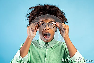 Unbelievable. Shocked black teen guy touching his glasses, opening his mouth, looking at camera on blue background Stock Photo