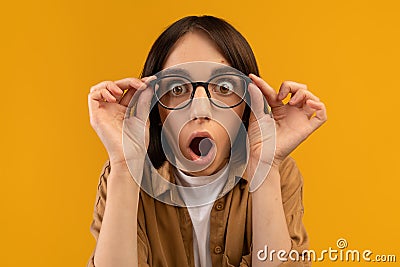 Unbelievable. Shocked caucasian lady touching glasses and looking at camera in shock, posing over yellow background Stock Photo