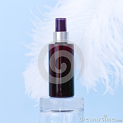 Unbranded brown sunscreen spray bottle on glass podium and large white ostrich feather on blue background. Blank label bottle for Stock Photo