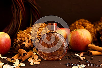 Unbranded perfume bottle, apples, cinnamon and dry hydrangea flowers on brown background. Spicy autumn scent. Transparent glass Stock Photo