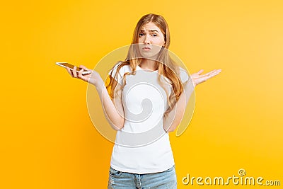 Uncertain woman with a phone in her hands, depicts misunderstanding and uncertainty on a yellow background Stock Photo