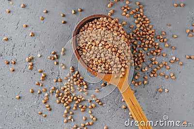 Uncooked brown buckwheat in wooden spoon against grey background. Organic food concept. Buckwheat grains. Ingredients for cooking Stock Photo