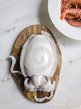 Uncooked Cuttlefish on wooden cutting board, shrimps in white ceramic plate - fresh seafood from above Stock Photo