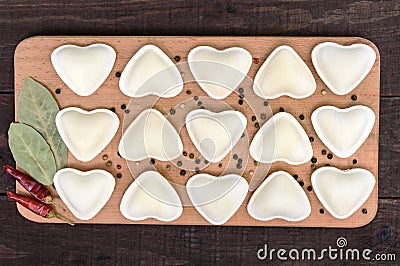 Uncooked dough in the shape of a heart dumplings, ravioli, pelmeni, on a cutting board. Stock Photo