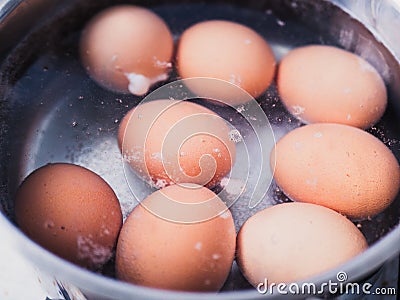 Uncooked eggs boiling in hot water in a silver pan Stock Photo