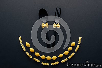 Uncooked farfalle pasta on plastic spoon and fork near shells macaroni and rotini pasta isolated on black. Stock Photo