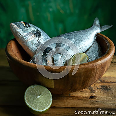 Uncooked fish with lime and herbs in a wooden bowl Stock Photo