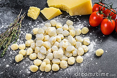 Uncooked homemade potato gnocchi with ingredients for cooking pasta. Black background. Top view Stock Photo