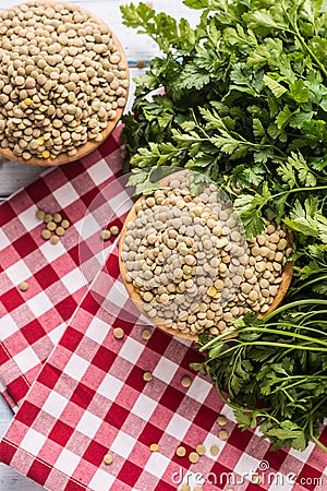 Uncooked lentils in wooden bowles with parsley herbs on kitchen table Stock Photo