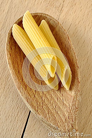 Uncooked penne pasta on a wooden spoon Stock Photo