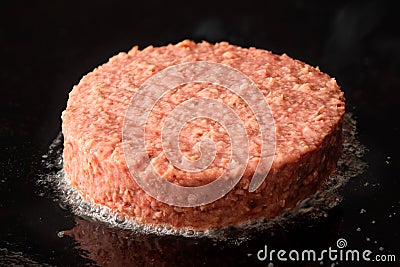 Uncooked plant based vegetarian burger patty being cooked on flat black iron grill Stock Photo