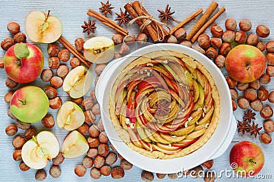 Uncooked tart tatin in the baking dish decorated with fresh sliced apples, hazelnuts, cinnamon sticks, anise stars. Homemade pie Stock Photo