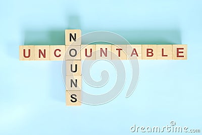 Uncountable nouns concept in English grammar noun education. Wooden block crossword puzzle flat lay in blue background. Stock Photo