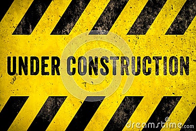 Under construction warning sign text with yellow black stripes painted over concrete wall cement facade texture background Stock Photo