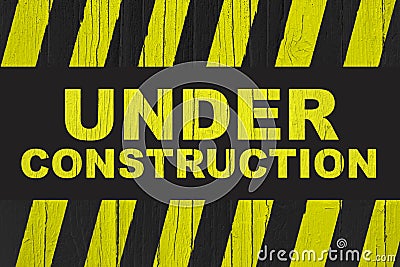 Under construction warning sign with yellow and black stripes painted over cracked wood. Stock Photo