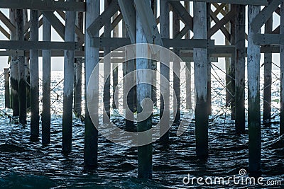 Under the Pier: Wooden Pillars and Crossbeams Over Sea Waters Stock Photo