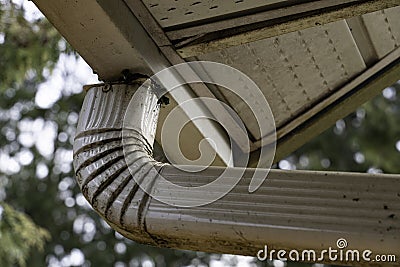 Underside of a dirty full exterior house gutter with downspout Stock Photo