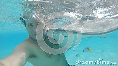 UNDERWATER: Cheerful man smiles while taking a selfie with a friendly stingray. Stock Photo