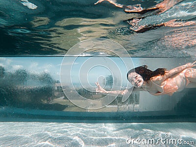 Underwater photo of aisan woman in bikini diving in the swimming pool with transparent glass wall. infinity pool edge on tropical Stock Photo