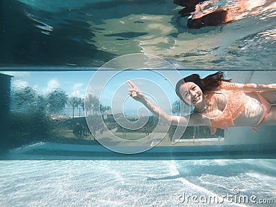 Underwater photo of aisan woman in bikini diving in the swimming pool with transparent glass wall. infinity pool edge on tropical Stock Photo