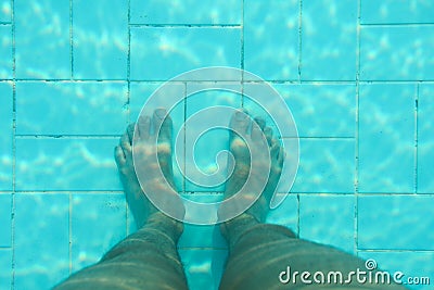 Underwater photo, bottom of swimming pool with blue tiles, man legs standing on it Stock Photo