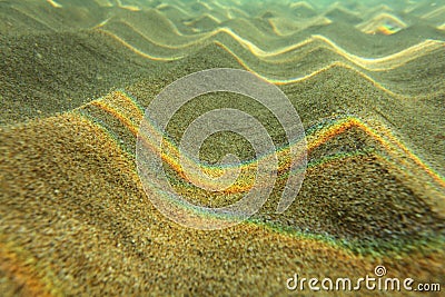 Underwater photo - light refracted on sea surface forming rainbows on small sand 