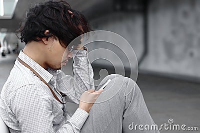 Unemployed stressed young Asian business man with hands on face and using mobile smart phone. Failure and layoff concept Stock Photo