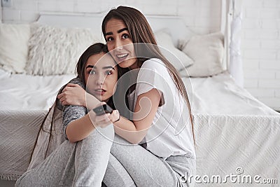 Unexpecter scary moment in the thriller movie. Sisters have fun watching TV while sits on the floor of beautiful bedroom Stock Photo