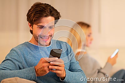 Unfaithful Boyfriend Chatting On Phone Sitting With Girlfriend At Home Stock Photo