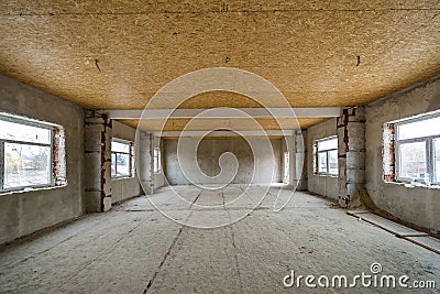 Unfinished apartment or house big loft room under reconstruction. Plywood ceiling, plastered walls, window openings, cement floor Stock Photo