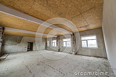 Unfinished apartment or house big loft room under reconstruction. Plywood ceiling, plastered walls, window openings, cement floor Stock Photo