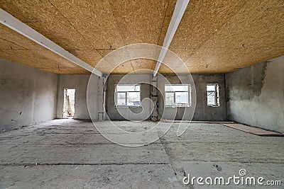 Unfinished apartment or house big loft room under reconstruction. Plywood ceiling, plastered walls, window openings, cement floor Stock Photo