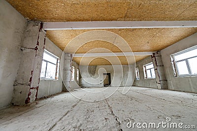 Unfinished apartment or house big loft room under reconstruction. Plywood ceiling, plastered walls, window openings, cement floor Stock Photo