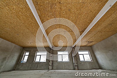 Unfinished apartment or house big loft room under reconstruction. Plywood ceiling, plastered walls, window openings, cement floor Stock Photo