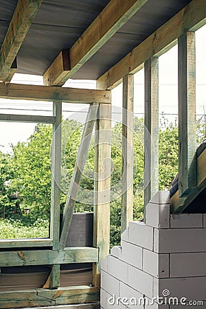 Unfinished attic wooden roof framing with vapor barrier, dormer and windows. View on timber rafters and beams on aerated concrete Stock Photo