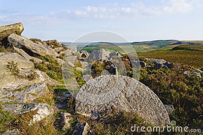 An unfinished millstone laying among rocks and heather on a Derbyshire hillside Stock Photo