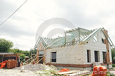 Unfinished modern farmhouse building. Wooden roof framing of mansard with dormer and aerated concrete block walls. Timber trusses Stock Photo