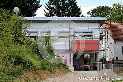 Unfinished small suburban family house surrounded with scaffolding and dense vegetation Stock Photo
