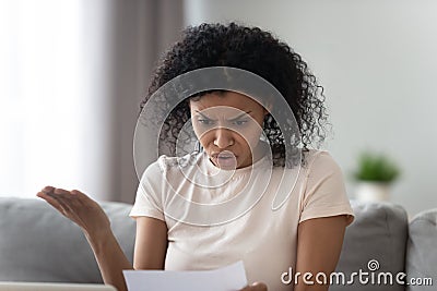 Unhappy angry African American woman reading paper letter, bad news Stock Photo