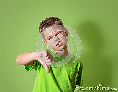 Unhappy, angry, displeased child giving thumbs down hand gesture, isolated on green background. Stock Photo