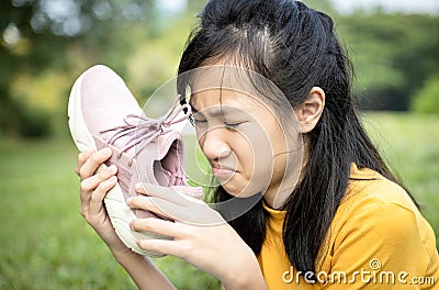 Unhappy asian female teenage is sniffing her sneakers,hold stinky shoe in her hand with disgust,unpleasant smell because of hot Stock Photo