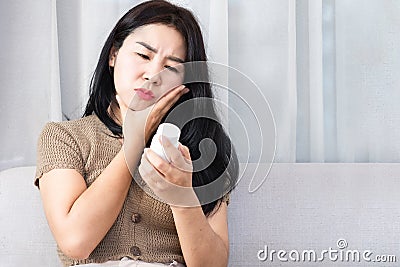 Unhappy Asian woman suffering from toothache, sore, swollen, and bleeding gums hand holding bottle of medidine Stock Photo