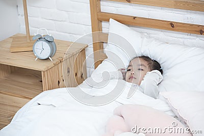 Unhappy or bad mood asian girl lay on bed hand cover ears from morning wake up clock Stock Photo
